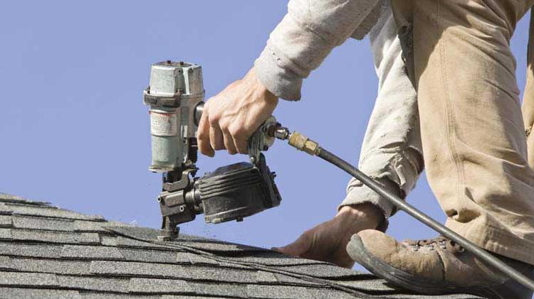 Man on roof fixing shingles with a nail gun.